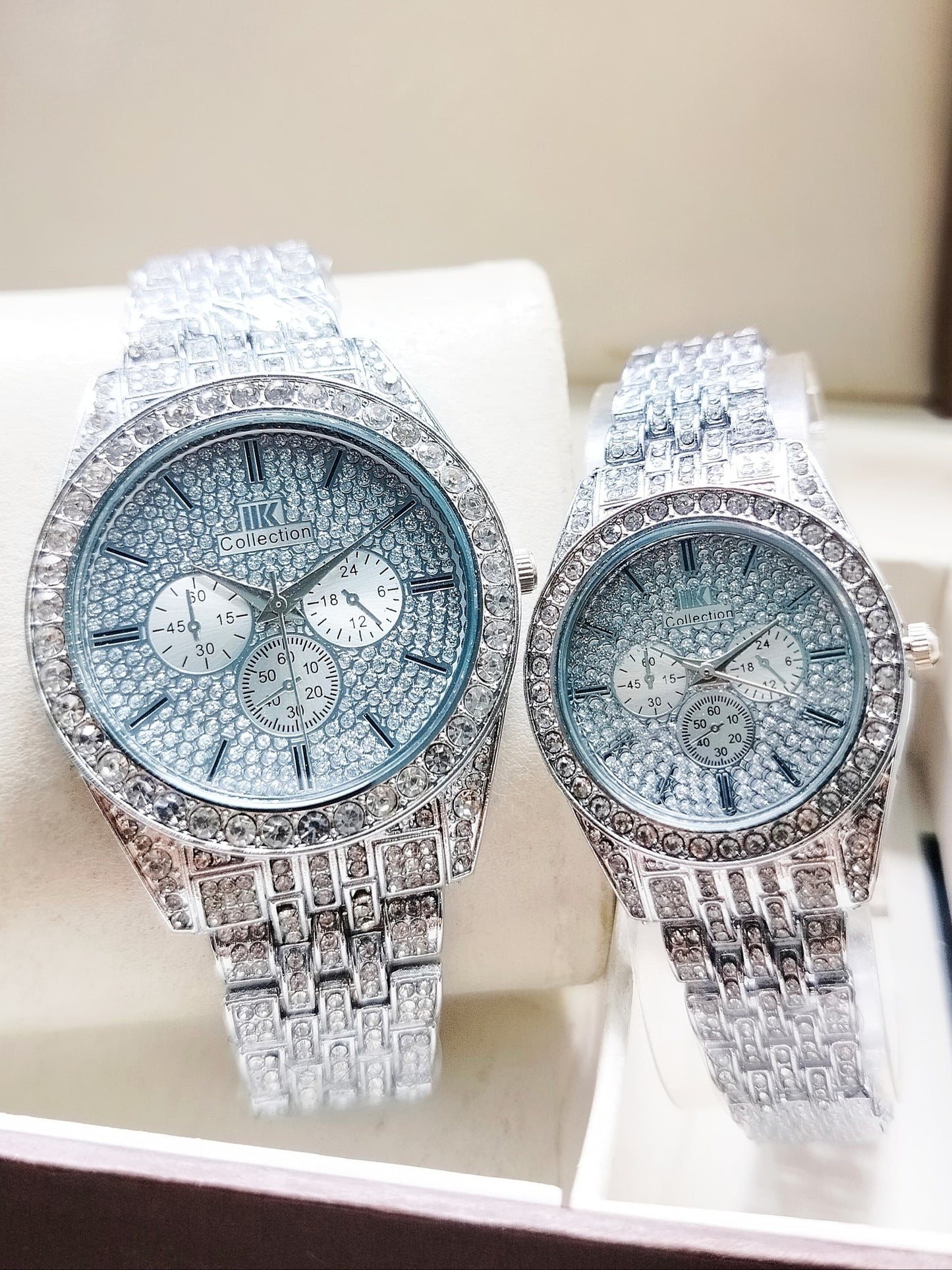 Two diamond-encrusted watches on a white cushion with a blurred background